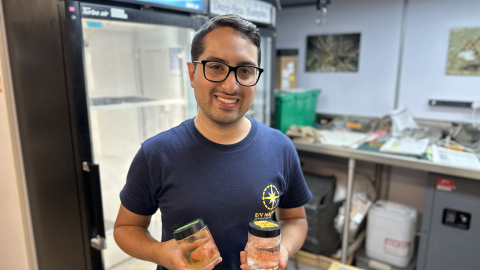 Sebastian Martinez stands in the Nautilus wetlab holding two samples jars and smiling