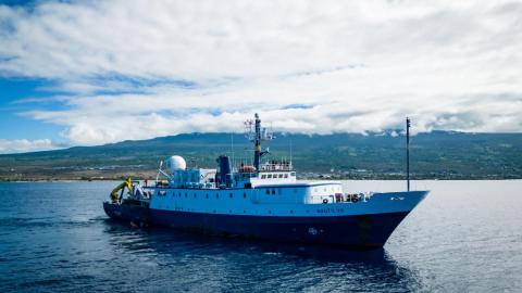 E/V Nautilus floats on a sunny day in front of an island in the background