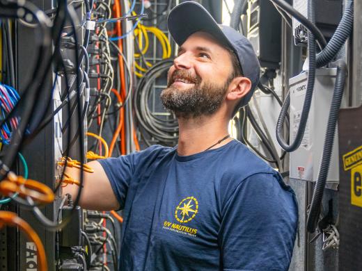 Data Engineer Julian stands smiling amid network cables and computer racks