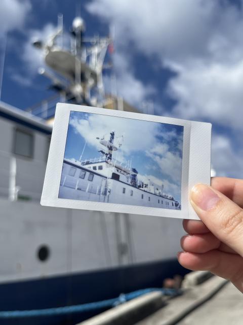 Hand holding a picture of a ship in front of the ship