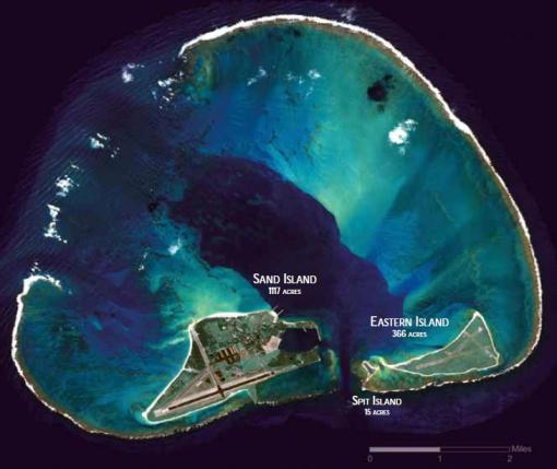 Satellite image of an atoll looking down at it. White fringing coral reef is visible in a ring with dark deep water outside that and shallow water inside