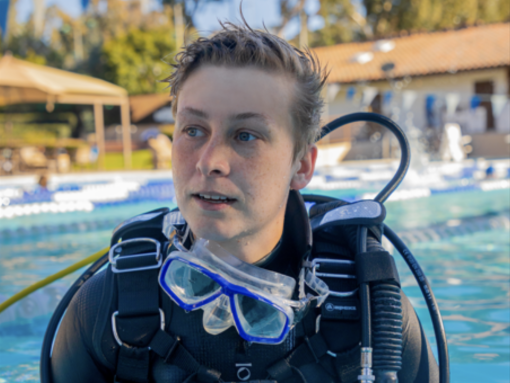 Nova emerges from a filming session, including a special camera housing to protect their camera and allow it to capture images clearly underwater. 