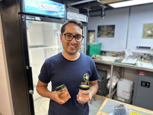 Sebastian Martinez stands in the Nautilus wetlab holding two samples jars and smiling