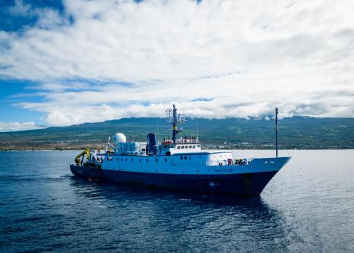 E/V Nautilus floats on a sunny day in front of an island in the background